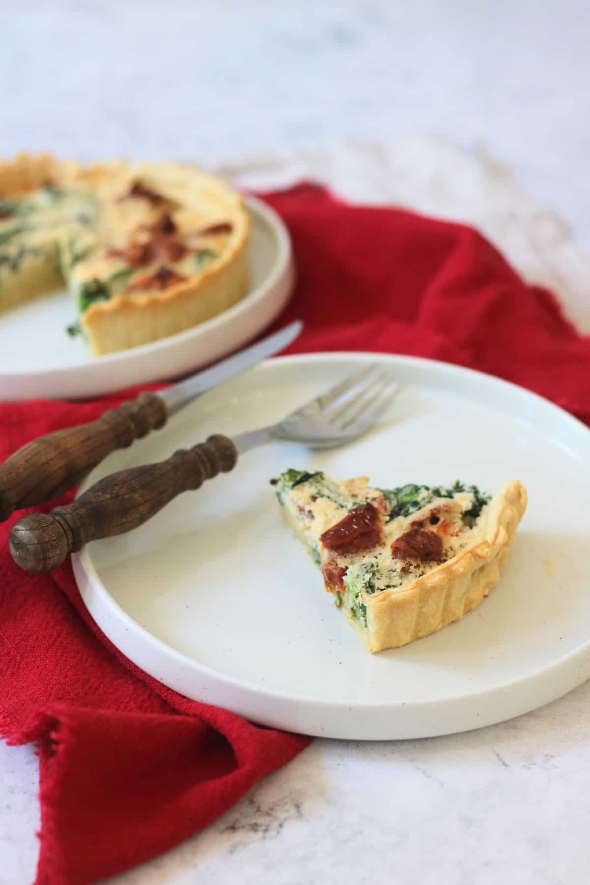 A slice of Vegan Tenderstem Broccoli and Sun-dried Tomato Quiche on a plate with red and cream napkin