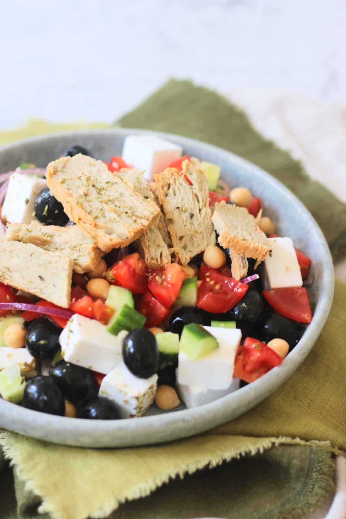 A plate of Greek Inspired Salad with Vegan Chicken Slices sat on green napkins