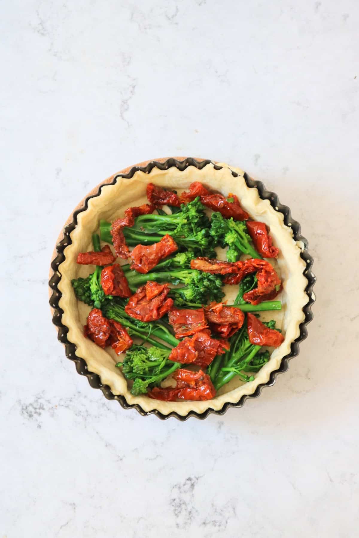 Tenderstem broccoli and sun-dried tomatoes in quiche pastry case ready for the egg-free filling to be poured over