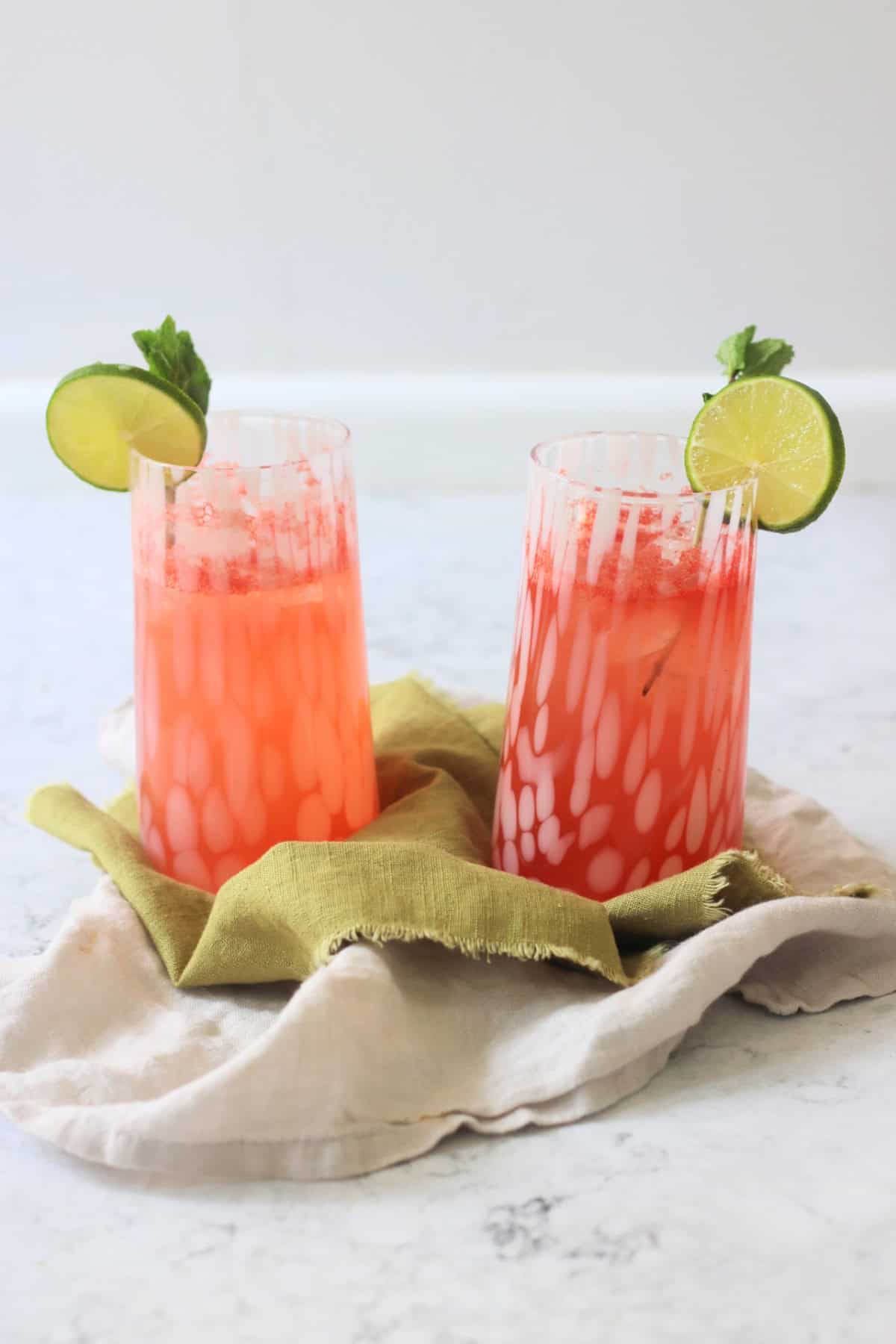 Two tall glasses of Watermelon Agua Fresca garnished with lime wheels and mint served on a green napkin