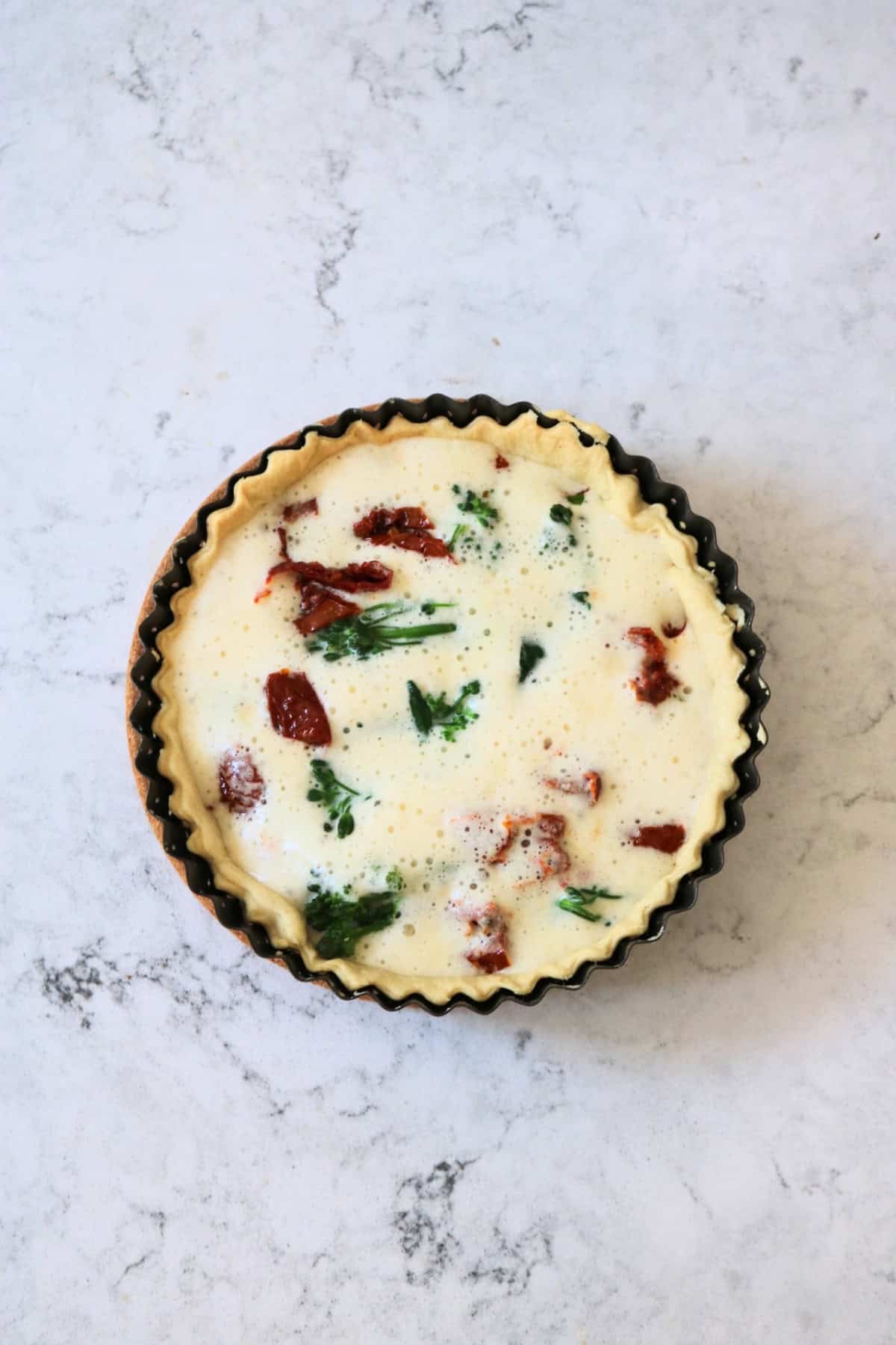 An uncooked Vegan Tenderstem Broccoli and Sun-dried Tomato Quiche, ready for the oven