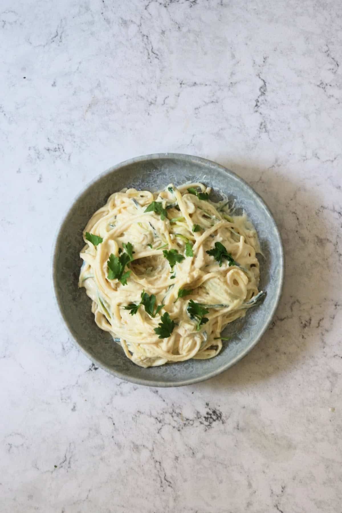 Vegan Creamy Courgette Linguine served on a blue plate with fresh parsley