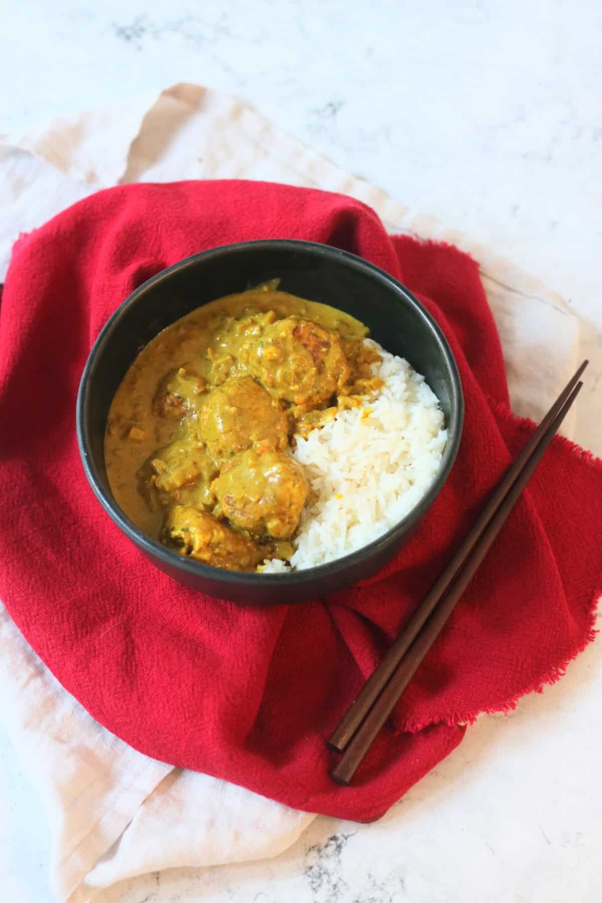 Hong Kong Style Vegan Curry Fish Balls served with white rice in a black bowl with a red napkin and wooden chopsticks