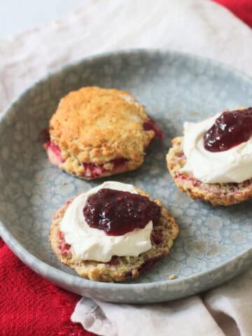 Vegan Raspberry and Lemon Scones on a plate topped with vegan cream and raspberry jam