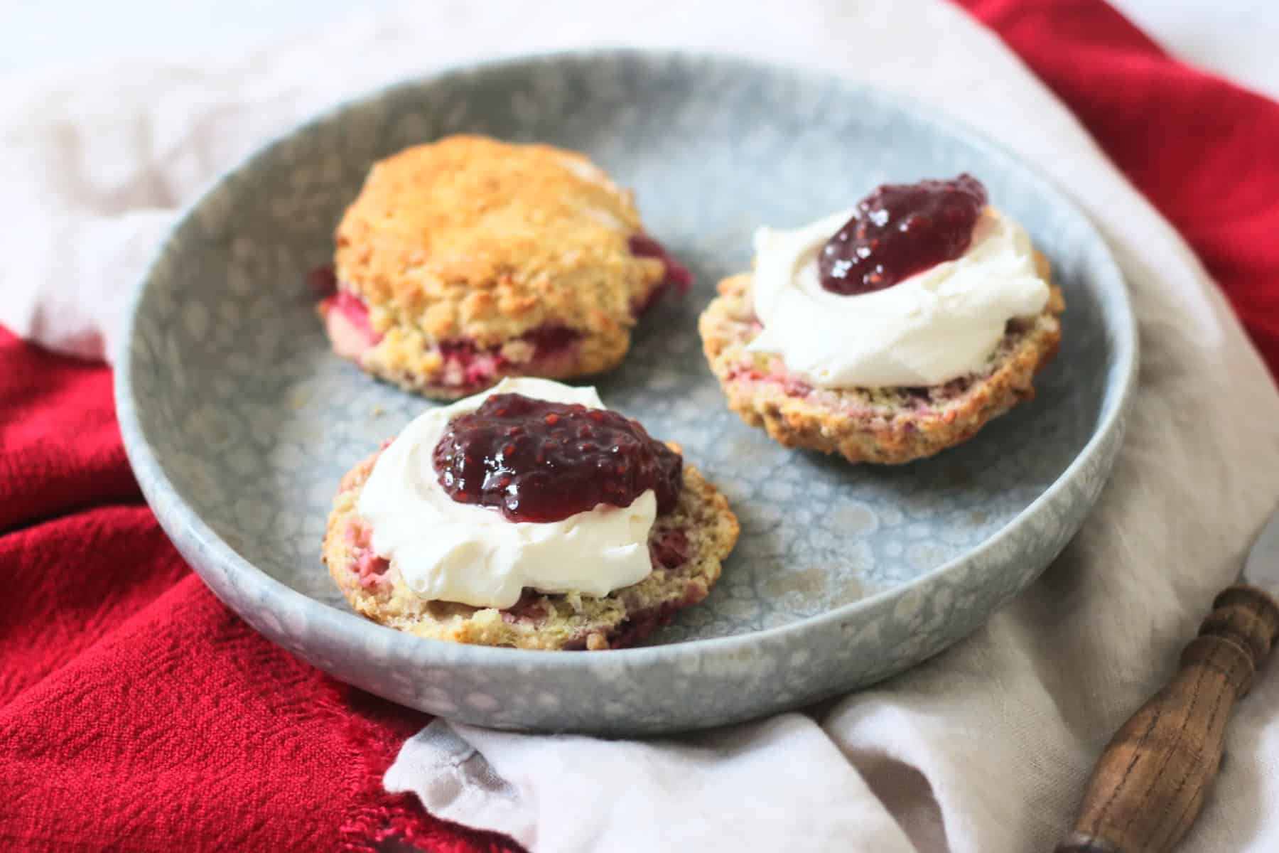 Vegan Raspberry and Lemon Scones on a plate topped with vegan cream and raspberry jam