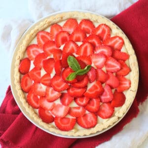 A whole Vegan Strawberry Tart (Vegan Tarte Aux Fraises) made up of a crisp pastry case, vegan creme patisserie and slices of strawberry topped with a couple of mint leaves.