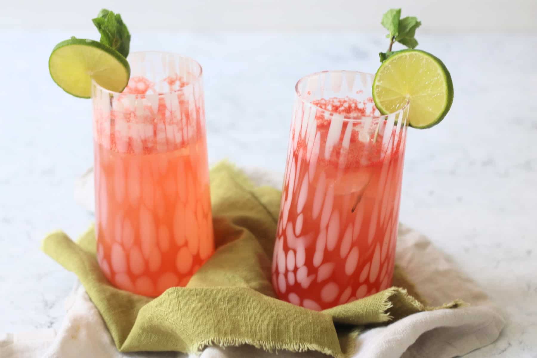 Two tall glasses of Watermelon Agua Fresca garnished with lime wheels and mint served on a green napkin
