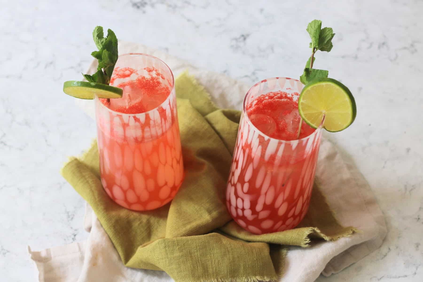 Two tall glasses of Watermelon Agua Fresca garnished with lime wheels and mint served on a green napkin