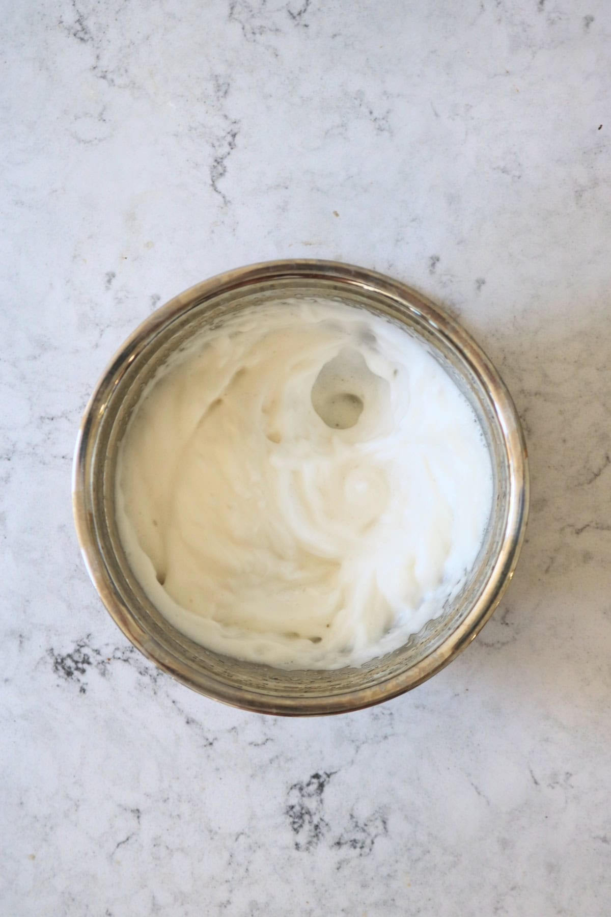 A mixing bowl containing aquafaba that has been whisked until forming soft peaks