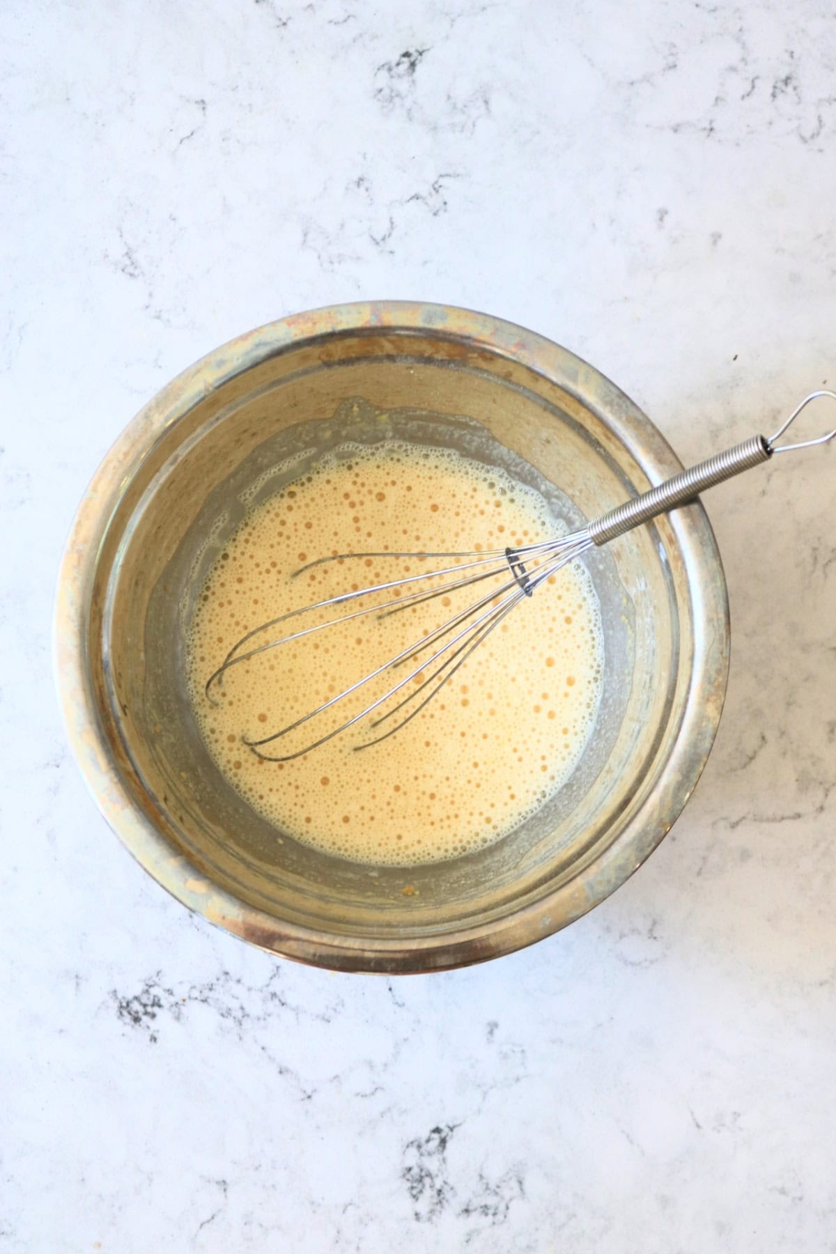 A batter made from chickpea flour in a metal mixing bowl with a whisk