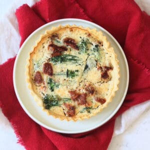 Whole Vegan Tenderstem Broccoli and Sun-Dried Tomato Quiche on a plate with red and cream napkins