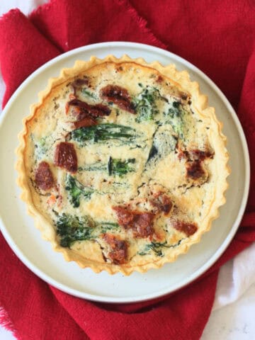 Whole Vegan Tenderstem Broccoli and Sun-Dried Tomato Quiche on a plate with red and cream napkins