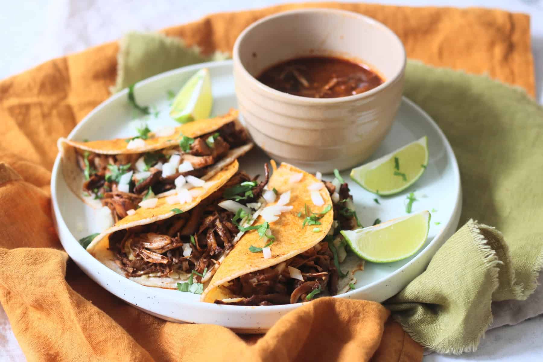 Oyster mushroom and jackfruit stuffed Vegan Birria Tacos topped with diced white onion and coriander and served with wedges of lime and cooking liquor to dip
