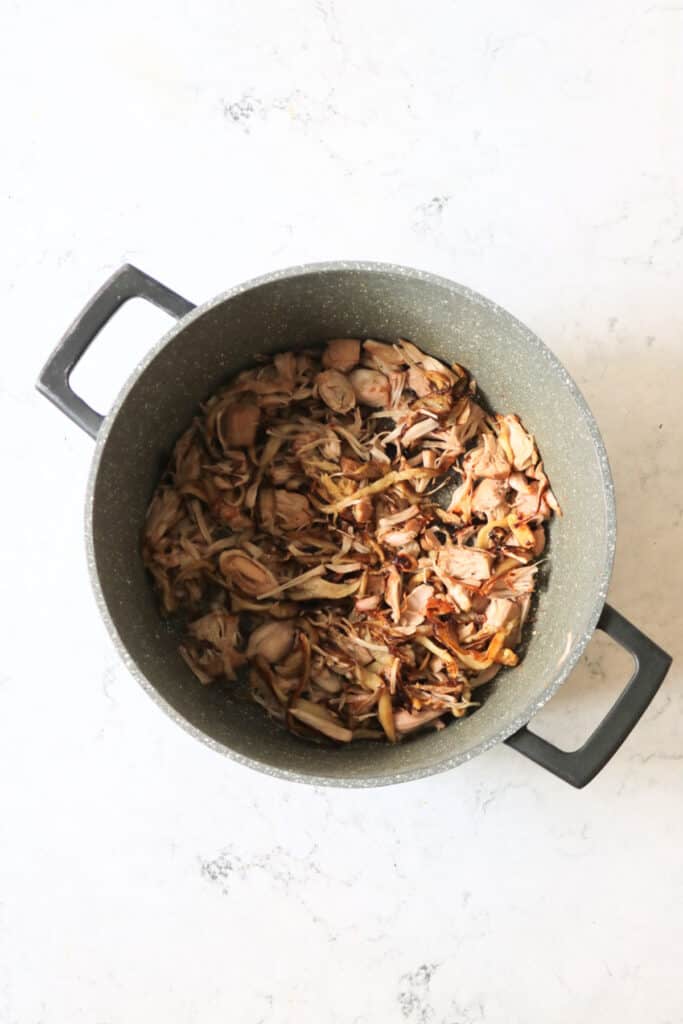 Shredded oyster mushrooms and jackfruit frying in a large heavy bottomed saucepan until they have crispy edges