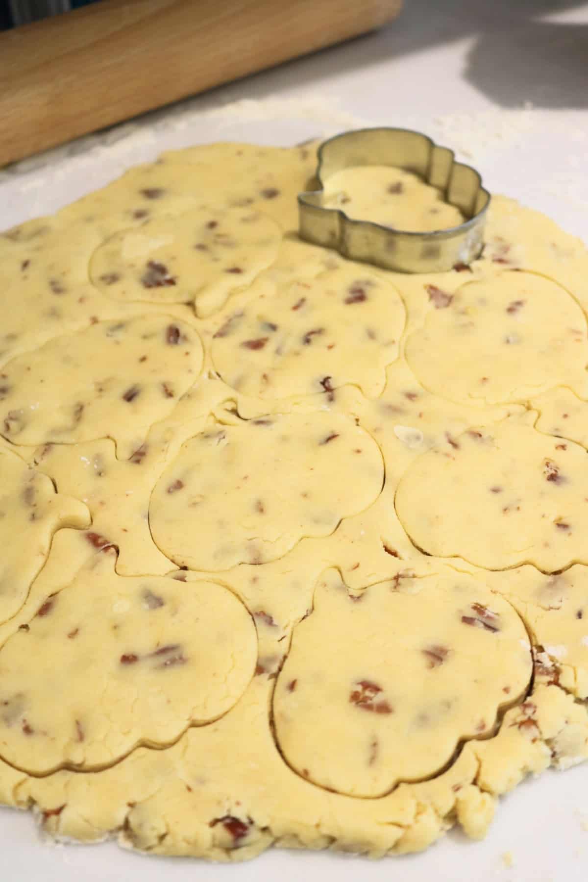 Vegan Pumpkin Spice and Pecan Cookie dough rolled out with pumpkin shapes being cut out using a pumpkin cookie cutter