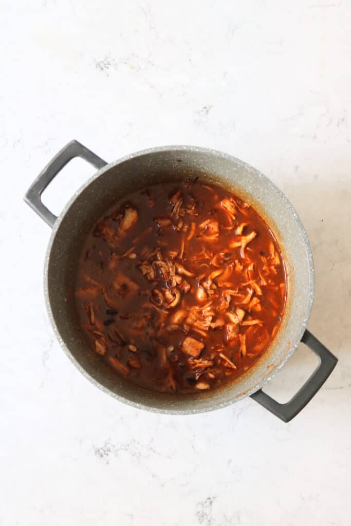The filling for birria tacos simmering in a large heavy bottomed saucepan