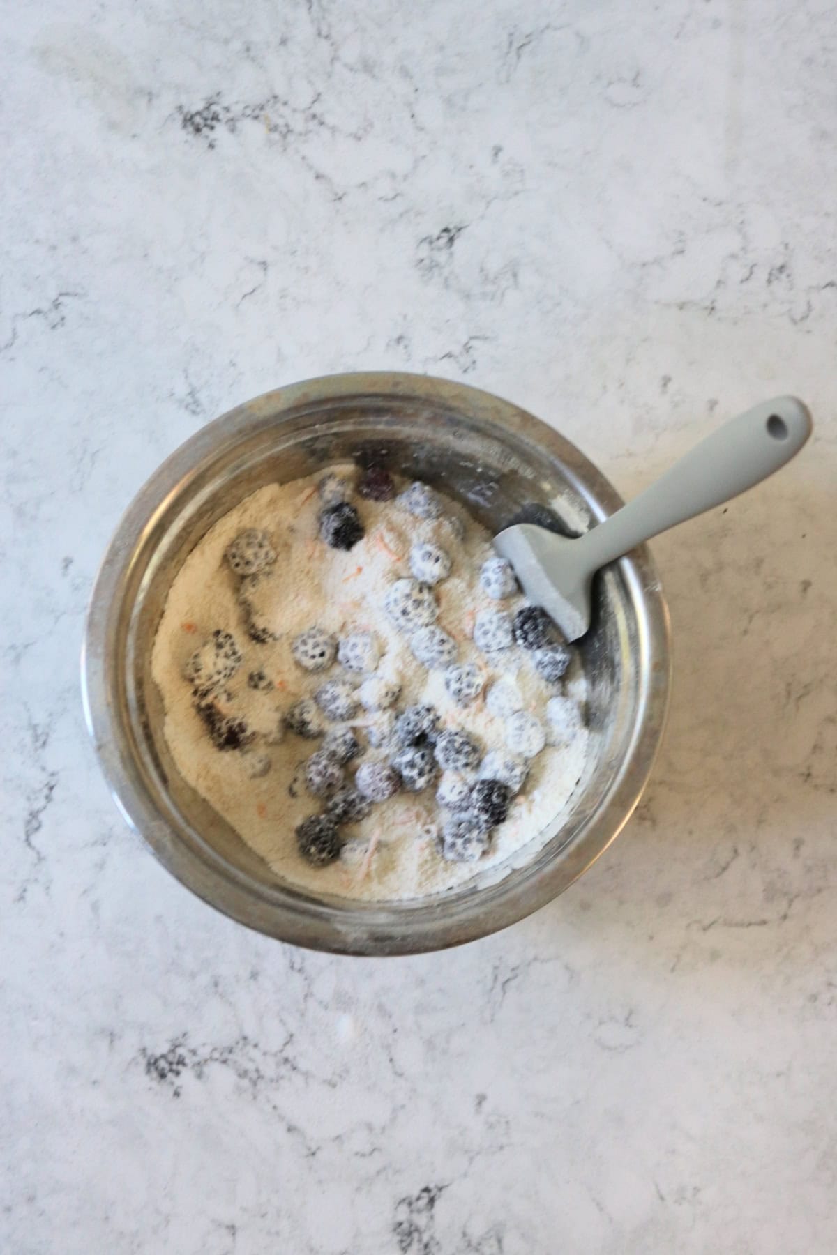 Mixing blackberries and dry ingredients for friand batter in a metal mixing bowl with a grey spatula