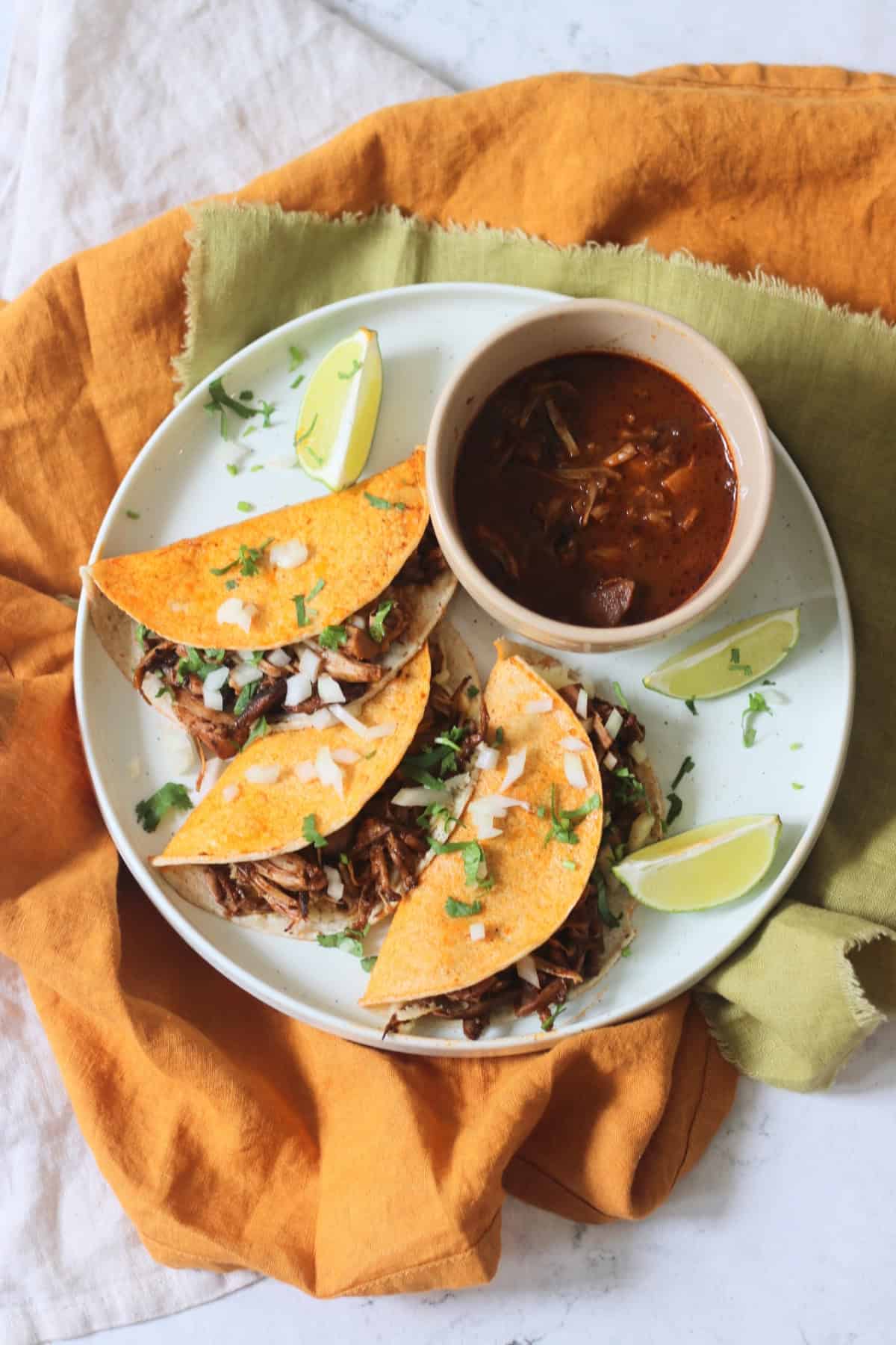 Oyster mushroom and jackfruit stuffed Vegan Birria Tacos topped with diced white onion and coriander and served with wedges of lime and cooking liquor to dip