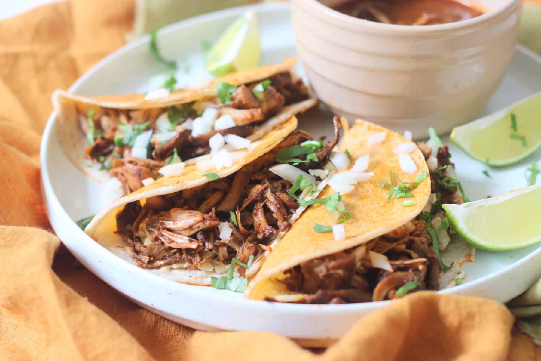 Oyster mushroom and jackfruit stuffed Vegan Birria Tacos served with diced white onion and coriander and wedges of lime