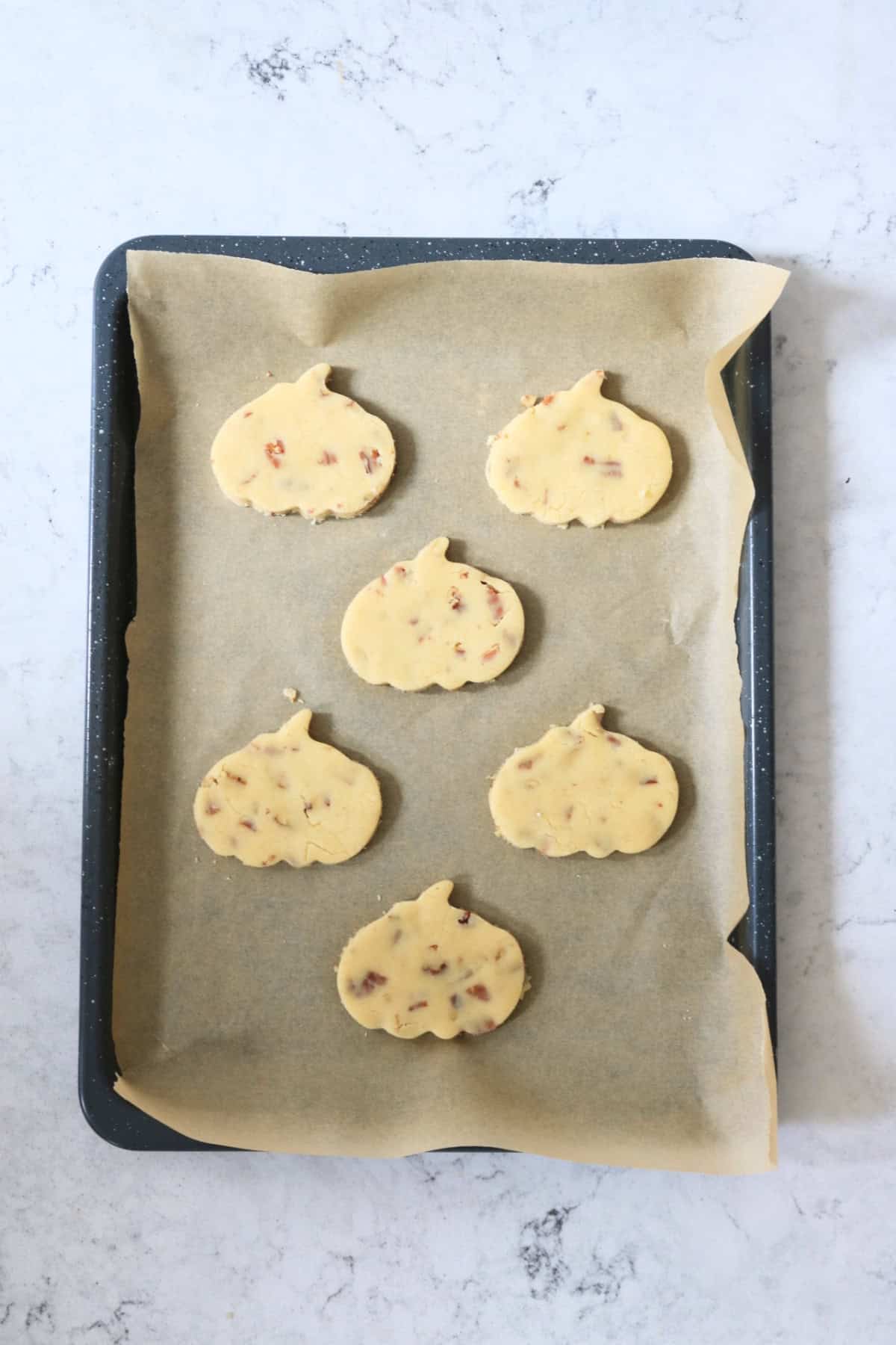 Pumpkins cut out of the Vegan Pumpkin Spice and Pecan Cookie dough, laid out on a baking sheet with baking paper, ready for the oven