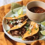 Oyster mushroom and jackfruit stuffed Vegan Birria Tacos topped with diced white onion and coriander and served with wedges of lime and cooking liquor to dip