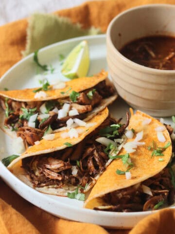 Oyster mushroom and jackfruit stuffed Vegan Birria Tacos topped with diced white onion and coriander and served with wedges of lime and cooking liquor to dip