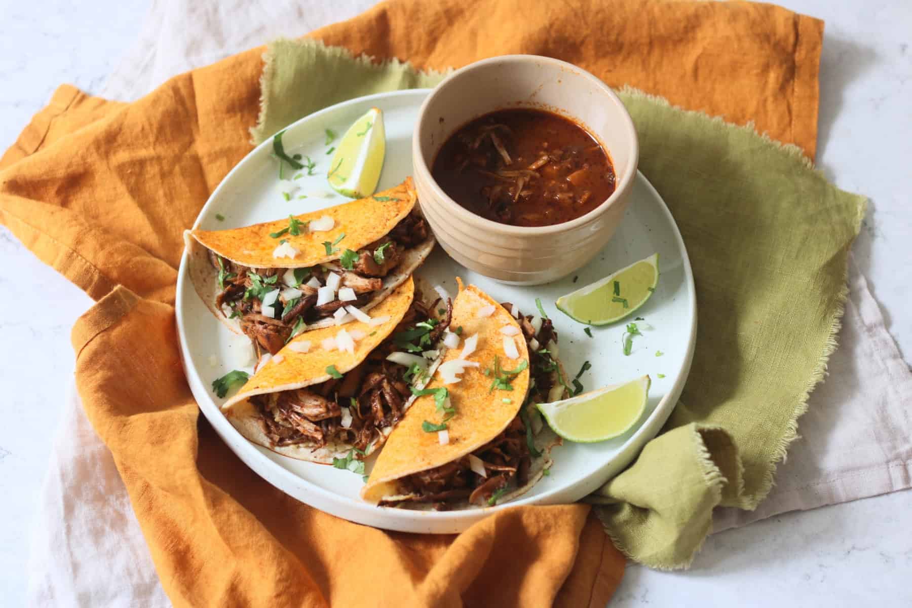 Oyster mushroom and jackfruit stuffed Vegan Birria Tacos topped with diced white onion and coriander and served with wedges of lime and cooking liquor to dip