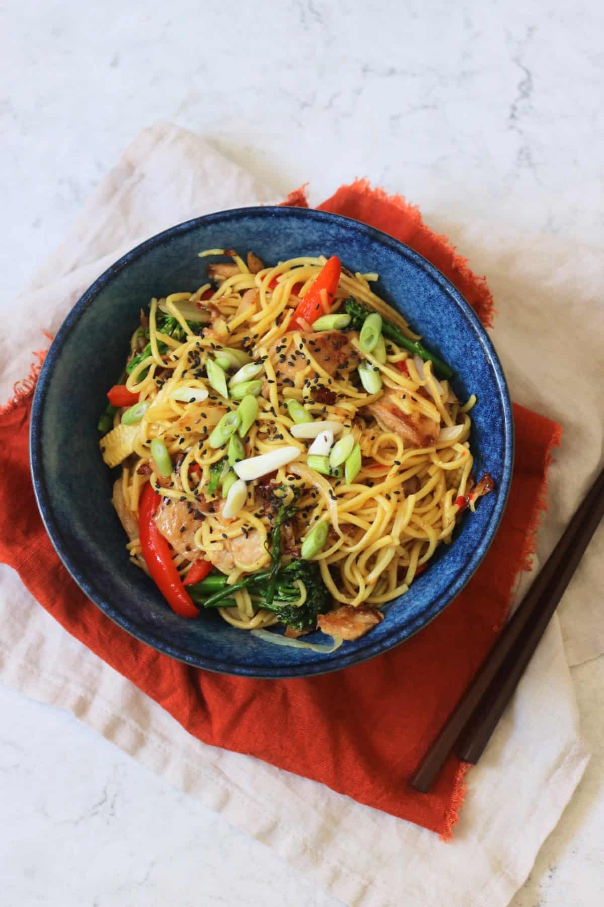 A bowl of Vegan Sweet Chilli Chicken Noodles on a red napkin with wooden chopsticks