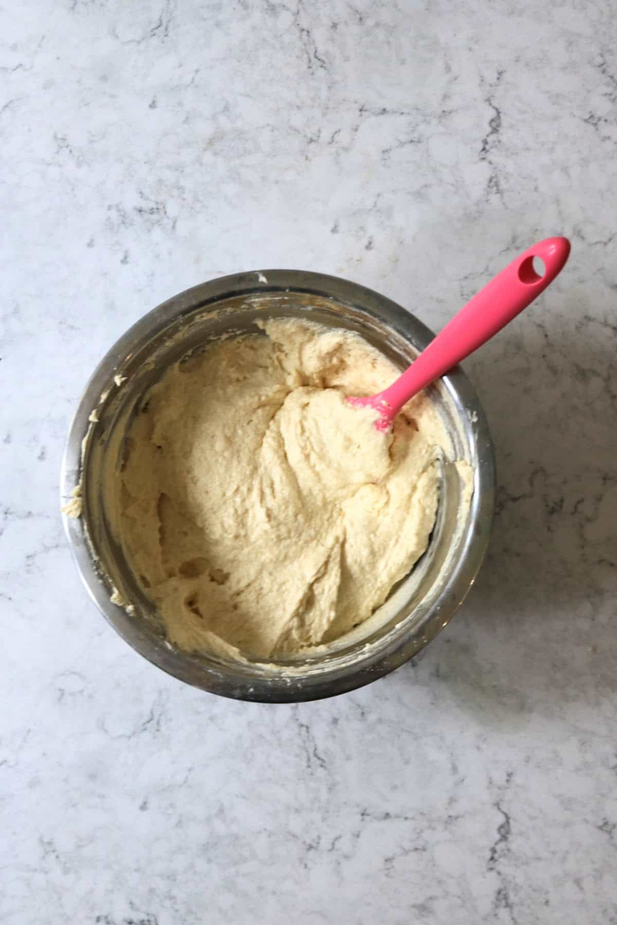 A bowl of vegan cupcake batter being stirred with a bright pink spatula