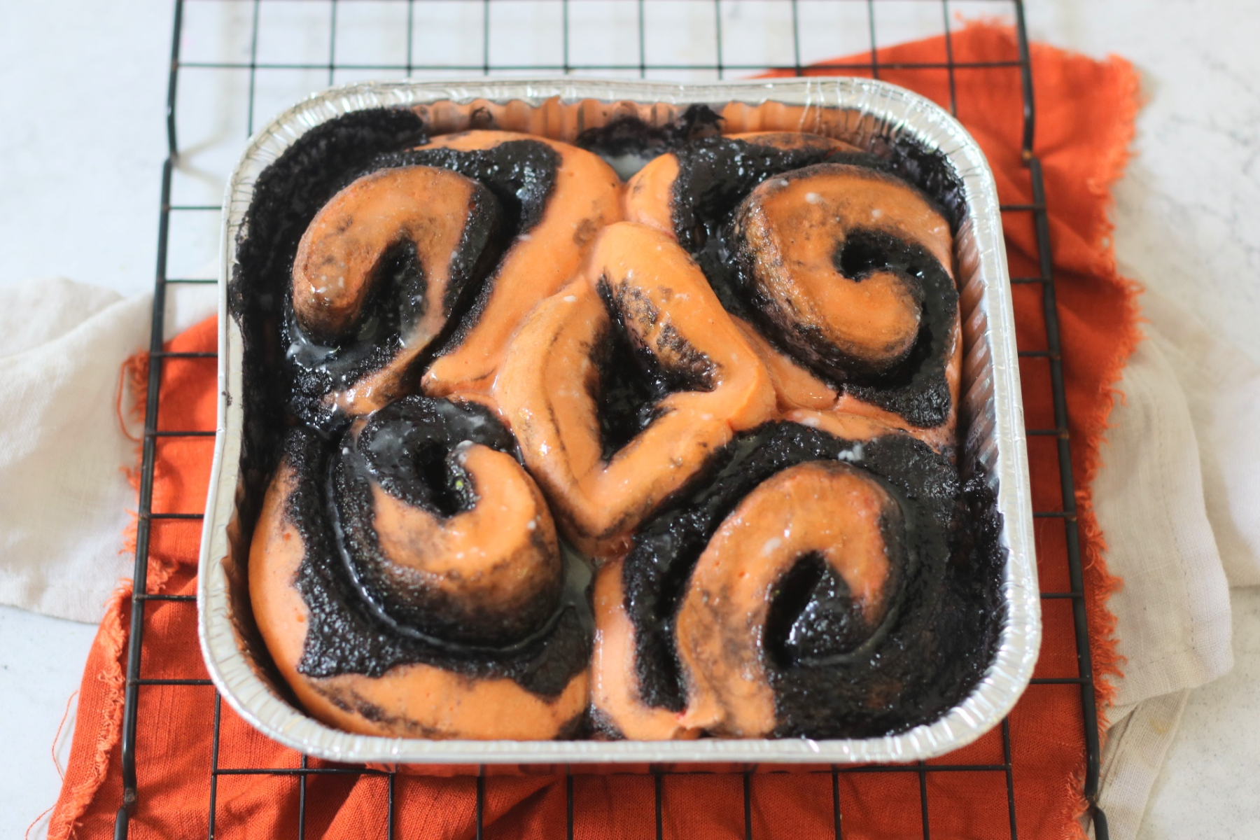 A tray of Vegan Halloween Pumpkin Spice Rolls glazed with vanilla icing sat on a wire rack