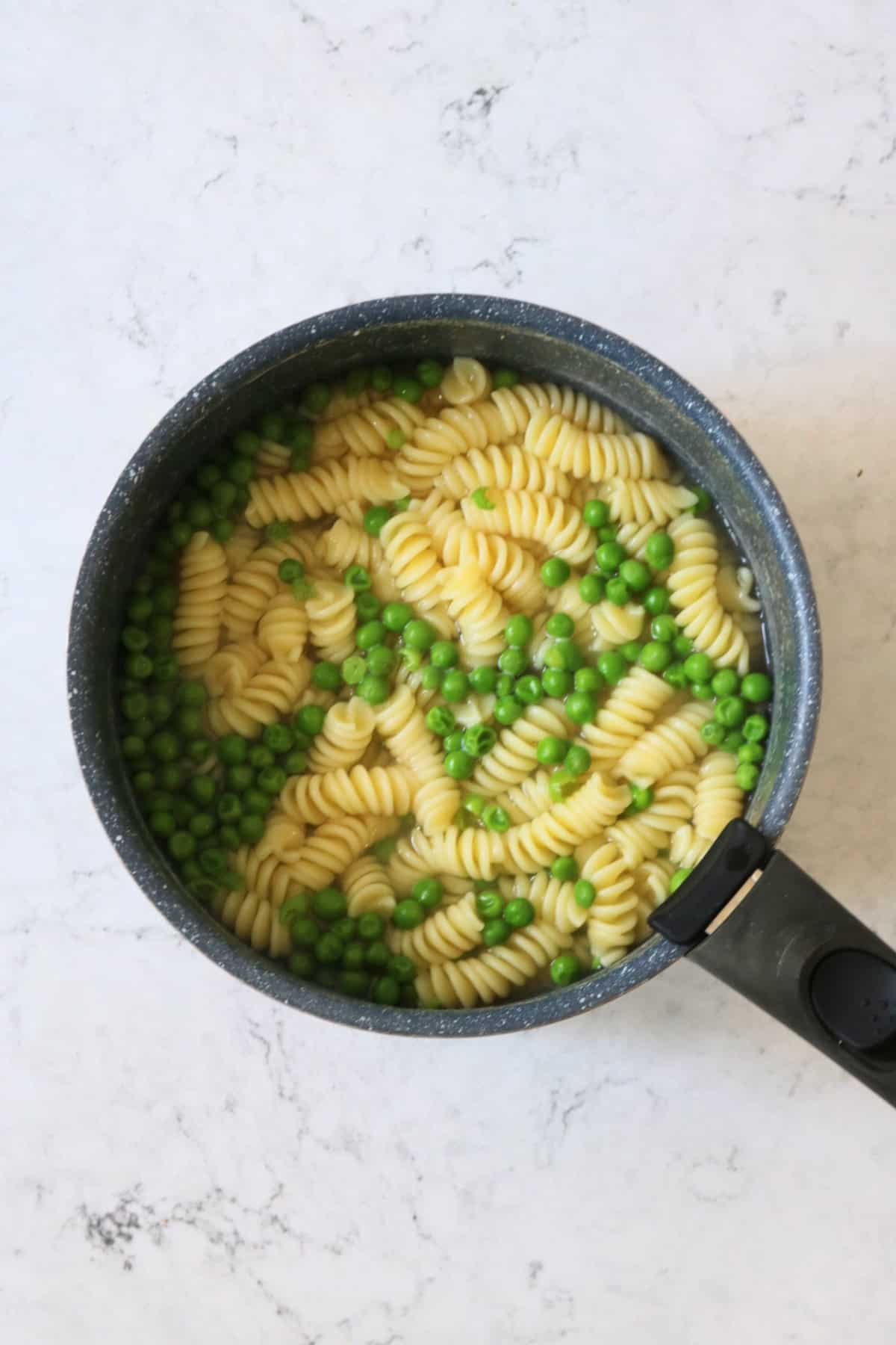 Peas added to a pan of pasta to cook through