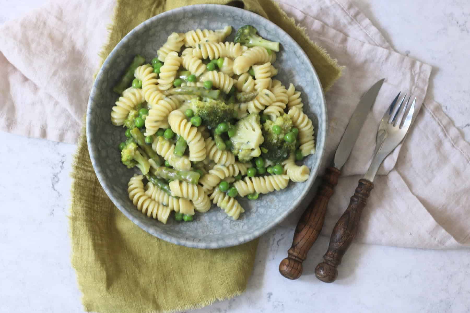 Vegan Blue Cheese Pasta with Spring Greens served with wooden handled knife and fork and a green napkin