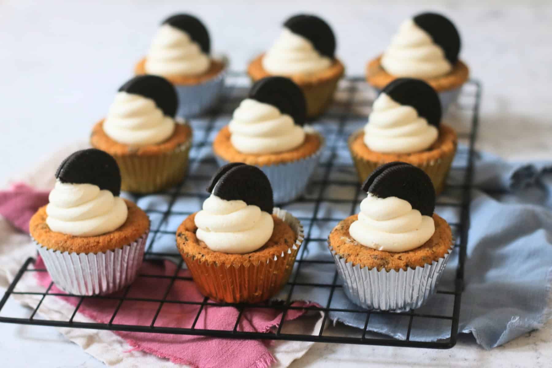 9 Vegan Oreo Cookies and Cream Cupcakes on a wire rack decorated with a swirl of buttercream and half an oreo