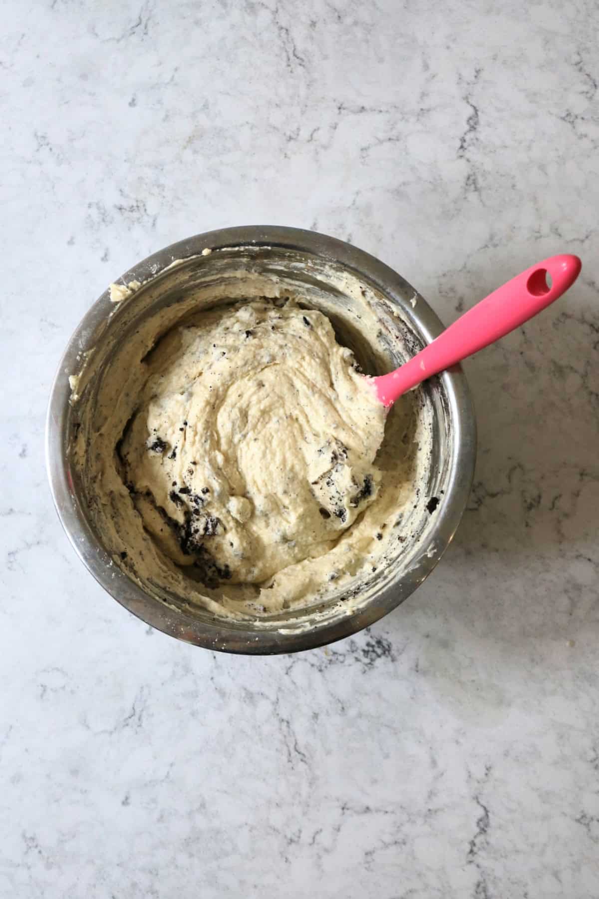 Folding crushed oreos into vegan cupcake batter with a bright pink spatula