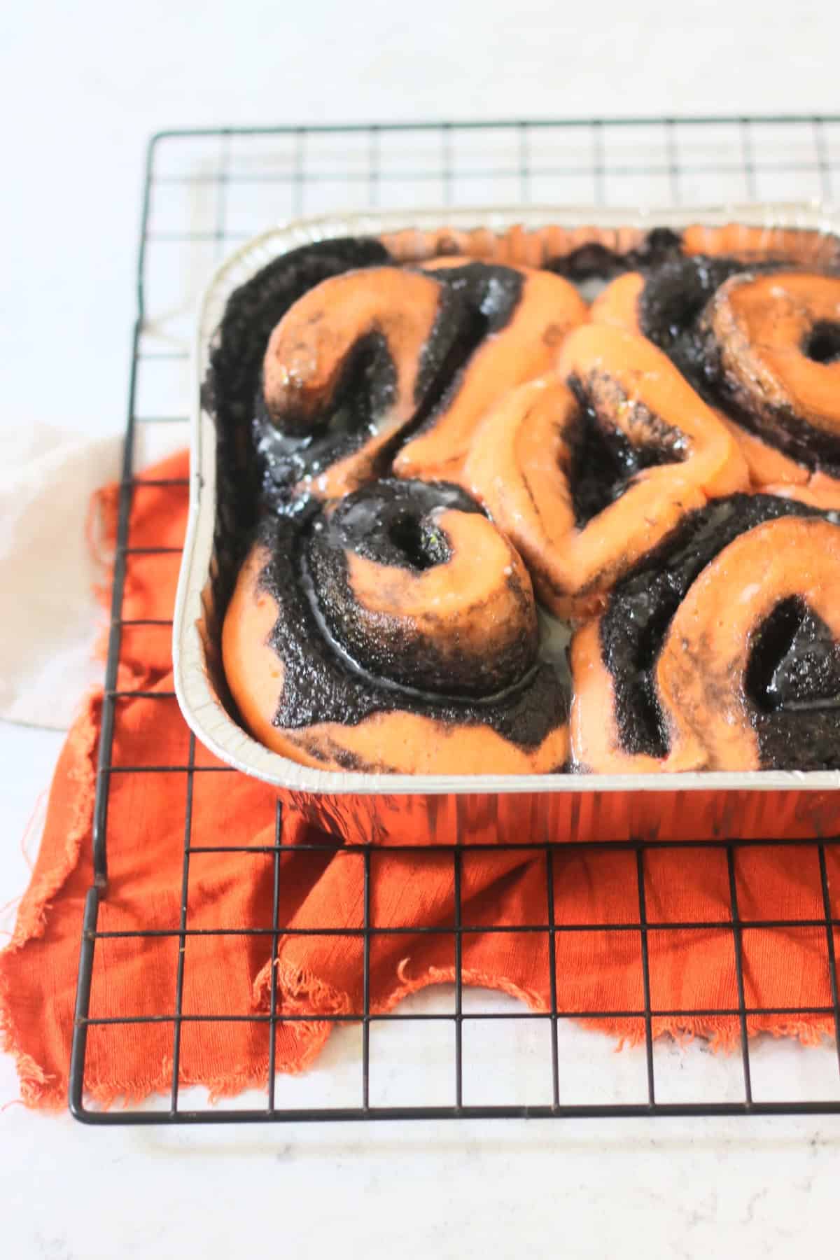 Glazed Vegan Halloween Pumpkin Spice Rolls in a foil tray sat on a wire rack