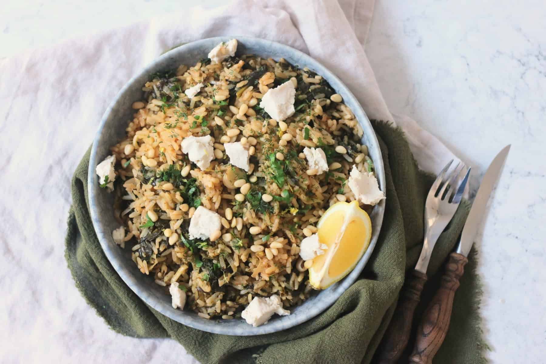 Greek Spinach Rice with Vegan Feta served on a plate with wooden handled cutlery and a green and cream napkin