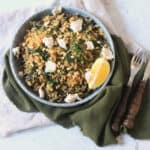 Greek Spinach Rice with Vegan Feta served on a plate with wooden handled cutlery and a green and cream napkin