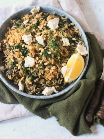 Greek Spinach Rice with Vegan Feta served on a plate with wooden handled cutlery and a green and cream napkin