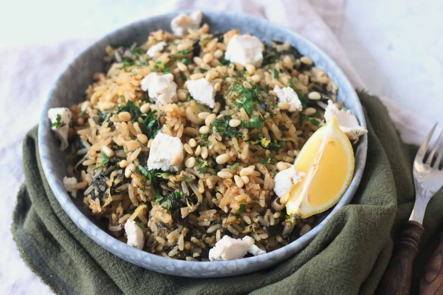 Greek Spinach Rice with Vegan Feta served on a plate with wooden handled cutlery and a green and cream napkin