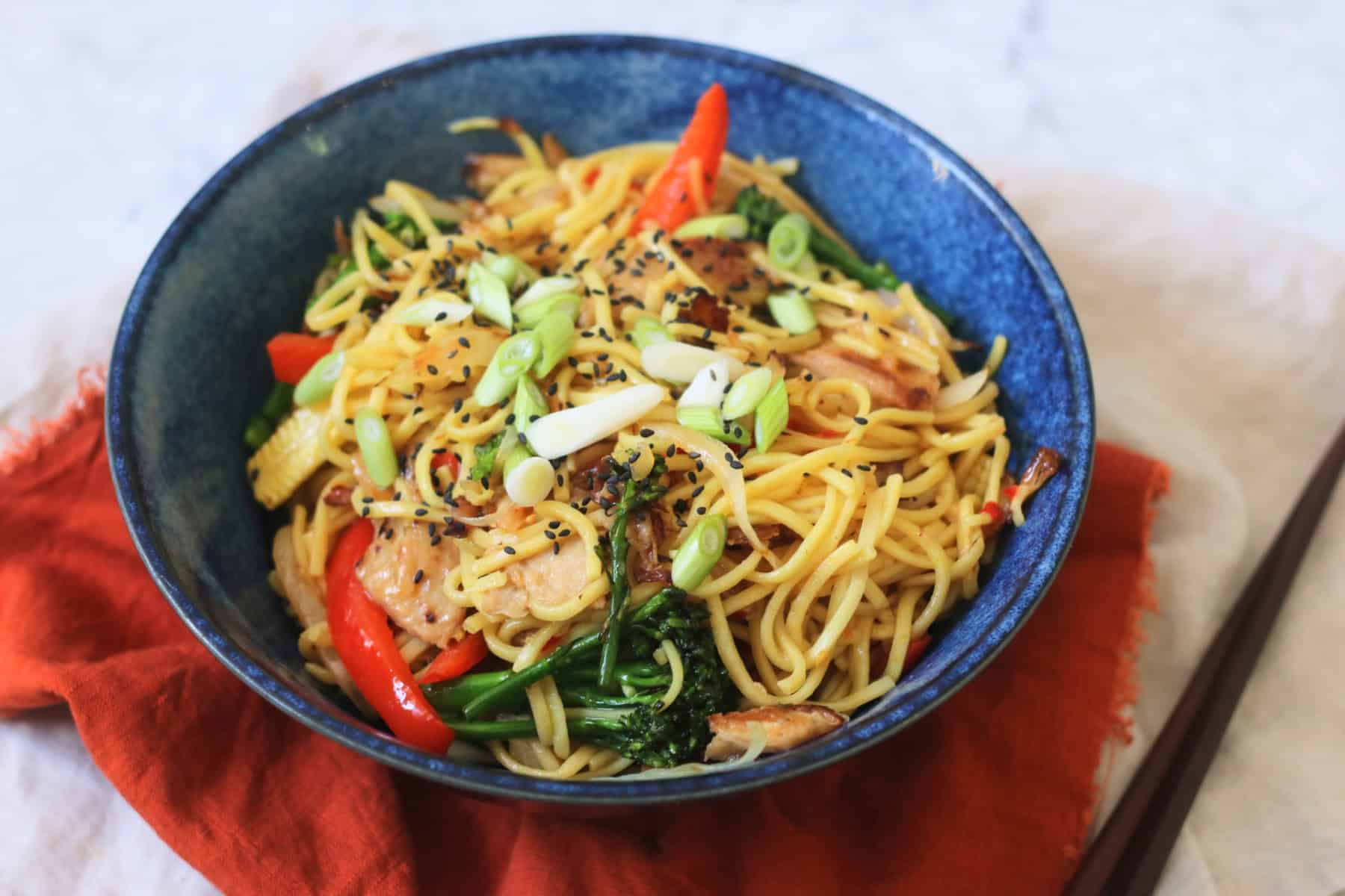 A bowl of Vegan Sweet Chilli Chicken Noodles on a red napkin with wooden chopsticks