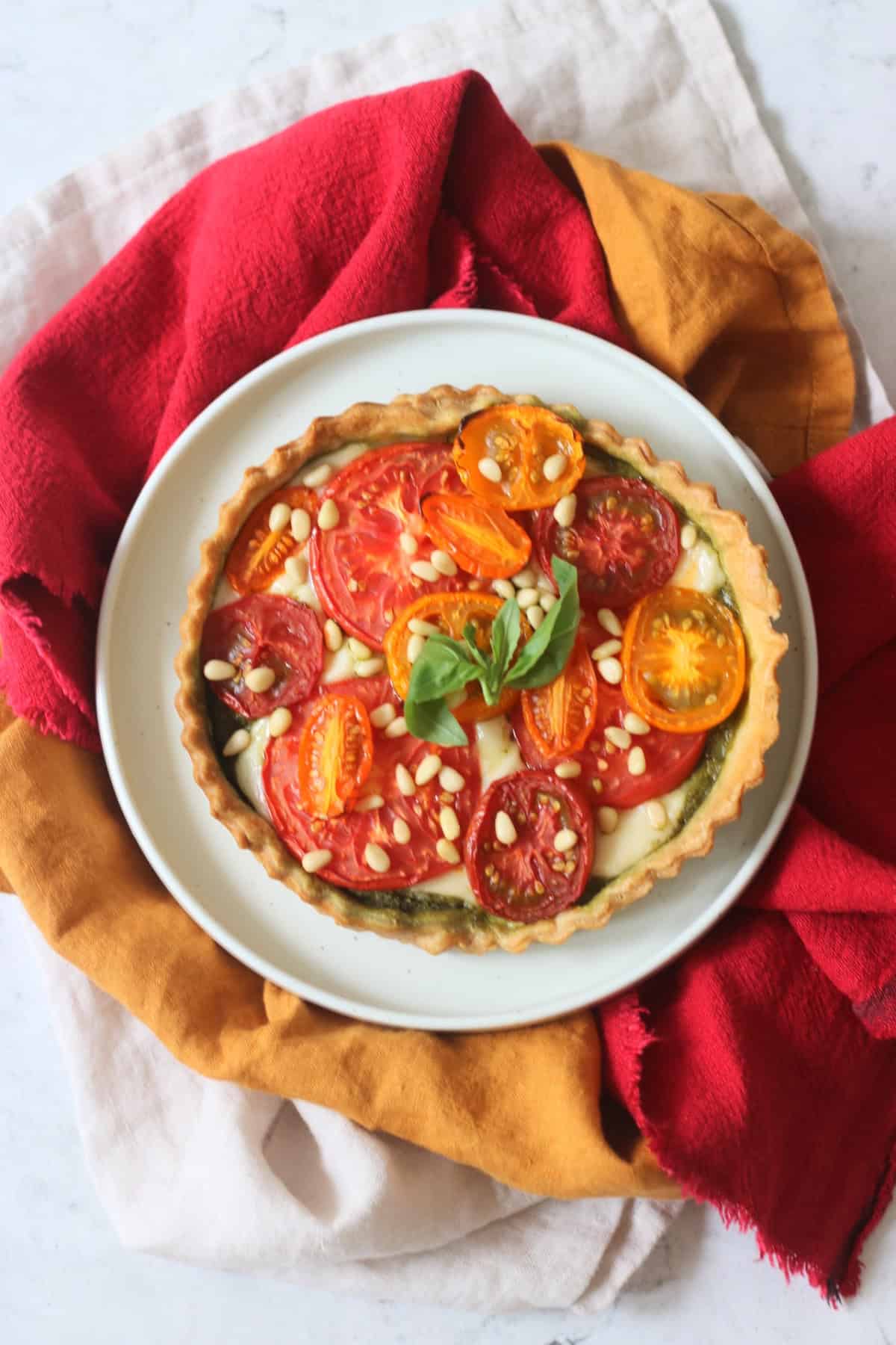 Plant Based Tomato Mozzarella and Pesto Picnic Tart on a plate with yellow and red napkins