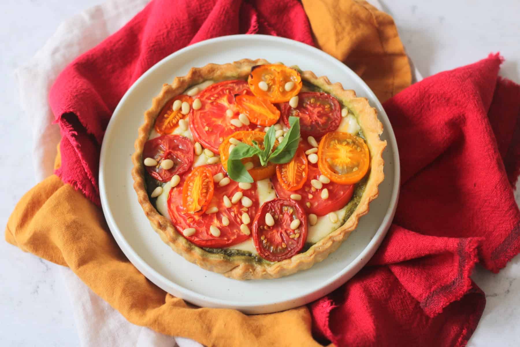 Plant Based Tomato Mozzarella and Pesto Picnic Tart on a plate with yellow and red napkins