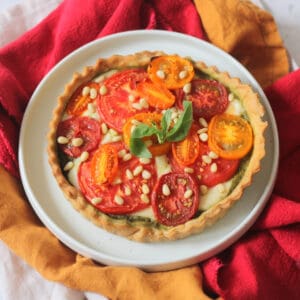 Vegan Tomato Mozzarella and Pesto Picnic Tart served on a white plate with red and yellow napkins