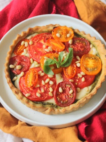 Vegan Tomato Mozzarella and Pesto Picnic Tart served on a white plate with red and yellow napkins