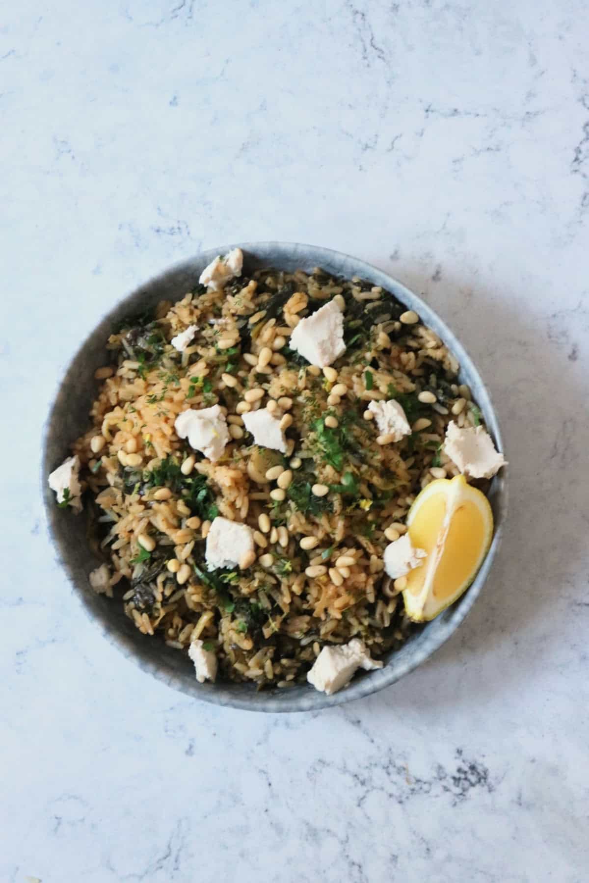 Greek Spinach Rice with Vegan Feta served on a plate with a wedge of lemon