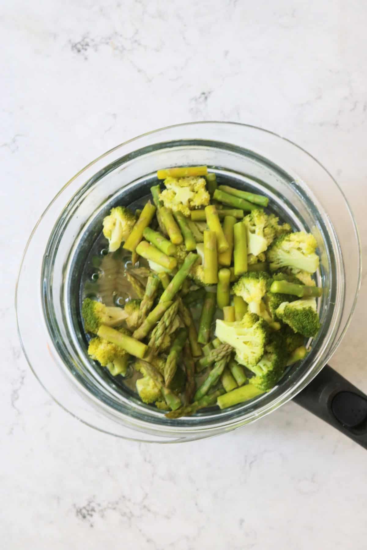 Steaming broccoli and asparagus above a pan of boiling water