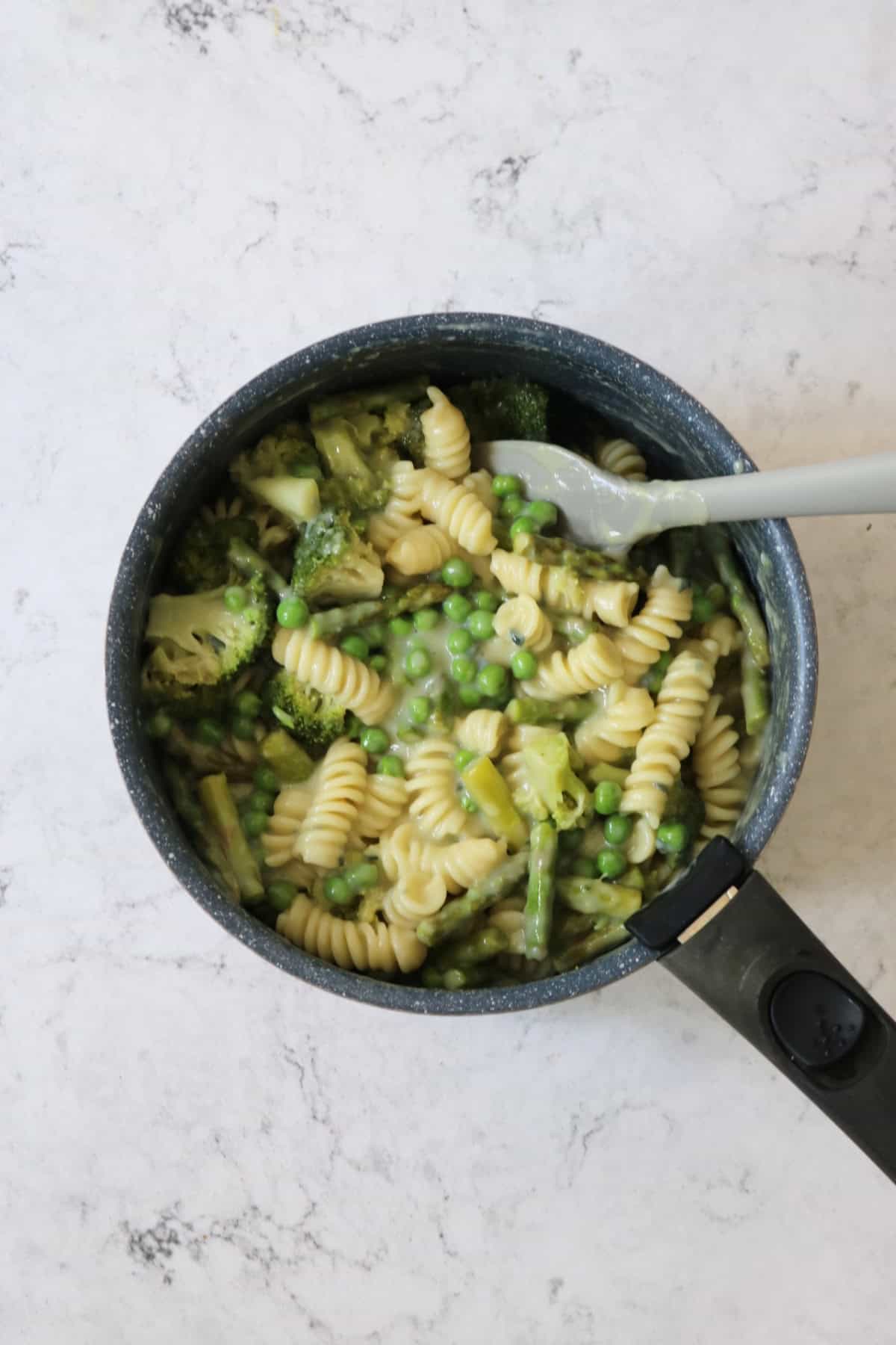 Stirring pasta, broccoli, asparagus, peas and vegan blue cheese sauce in a pan