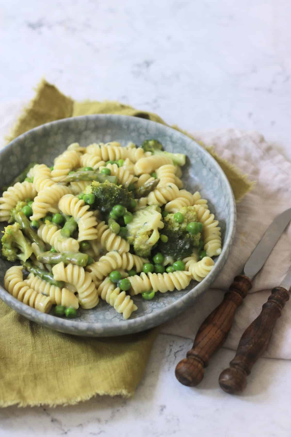 Vegan Blue Cheese Pasta with Spring Greens served with wooden handled knife and fork and a green napkin