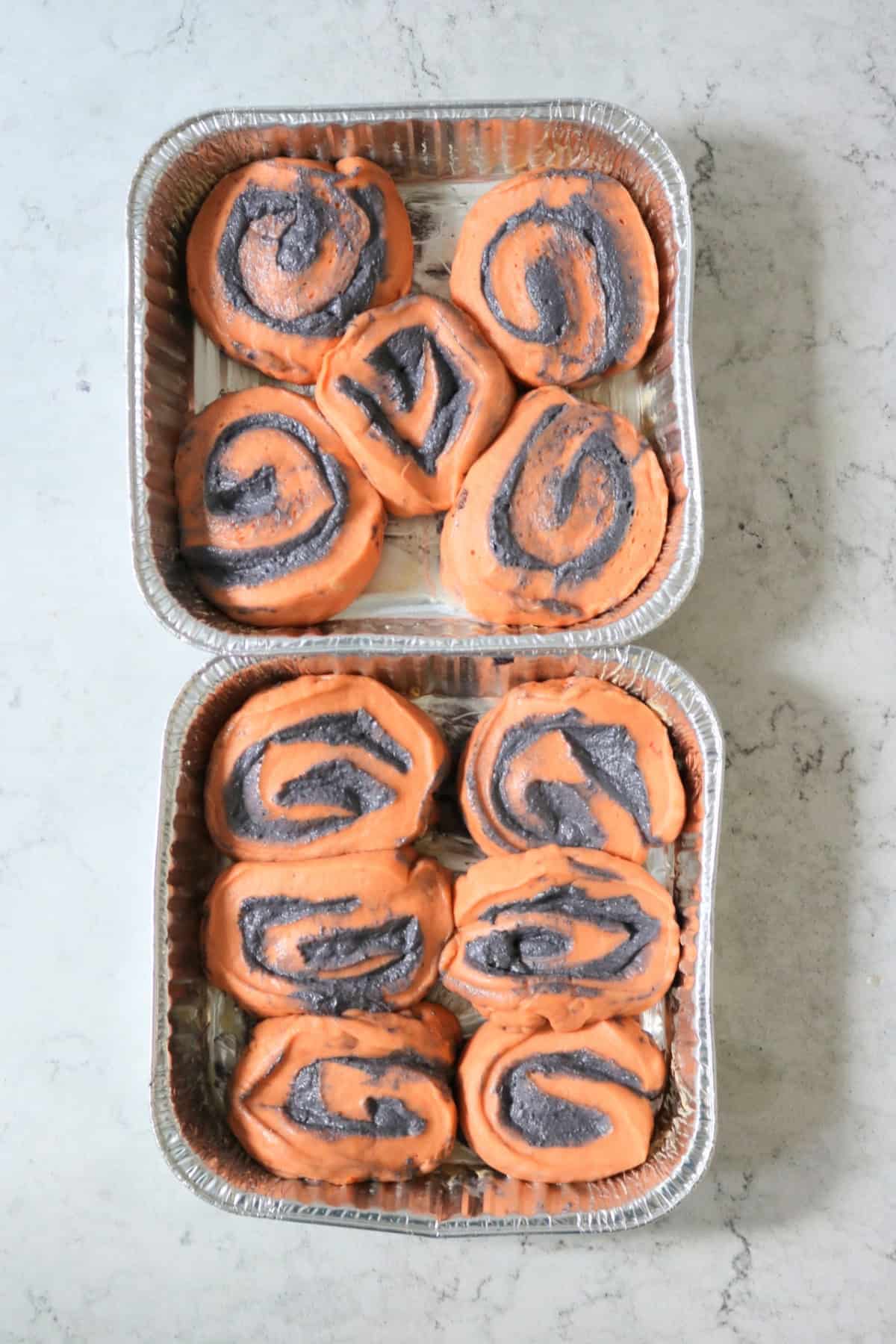 Two tin foil trays of Vegan Halloween Pumpkin Spice Rolls ready for the oven