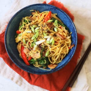 A bowl of Vegan Sweet Chilli Chicken Noodles on a red napkin with wooden chopsticks